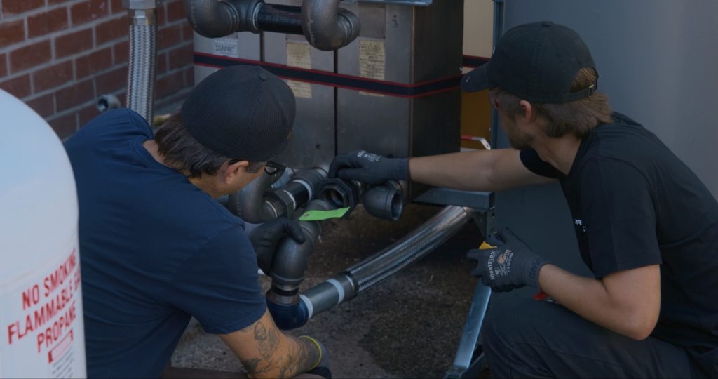 Two Critical Energy technicians connecting piping to a heat exchanger unit at an installation site