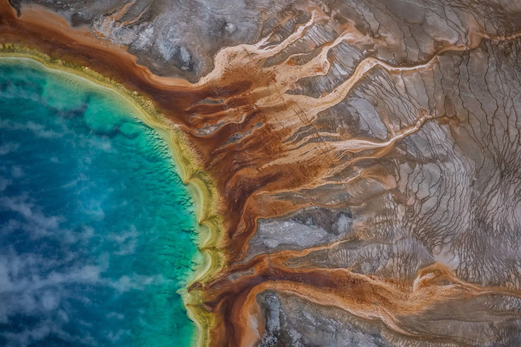 Aerial view of a hot spring with bands of orange and turquoise mineral deposits