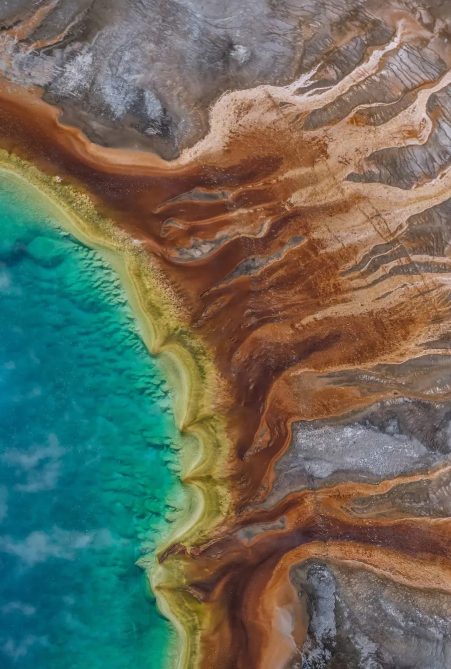 Aerial view of a hot spring with bands of orange and turquoise mineral deposits